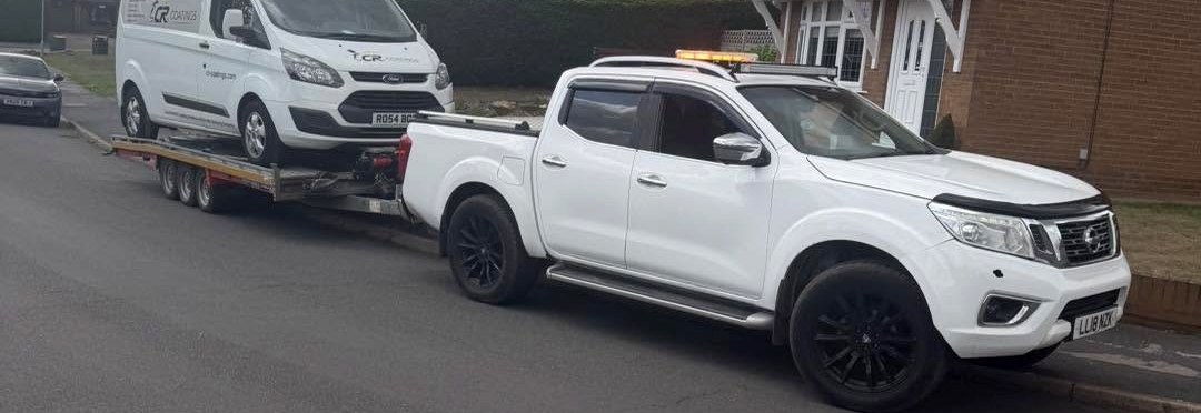 Nissan recovery pickup towing a white van on a trailer